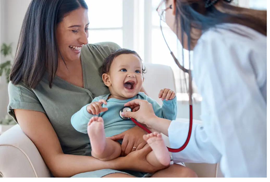 A mother holding her smiling baby during a pediatrician visit, capturing the warmth of family-centered healthcare